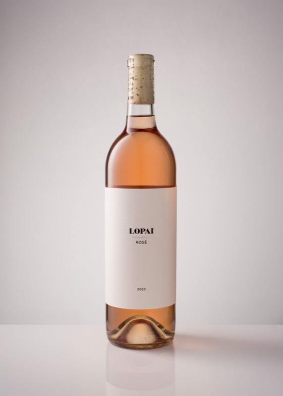 A tall, slender bottle of rosé wine with a white label that reads 'LOPAI ROSÉ 2023', standing on a white surface against a plain light background.